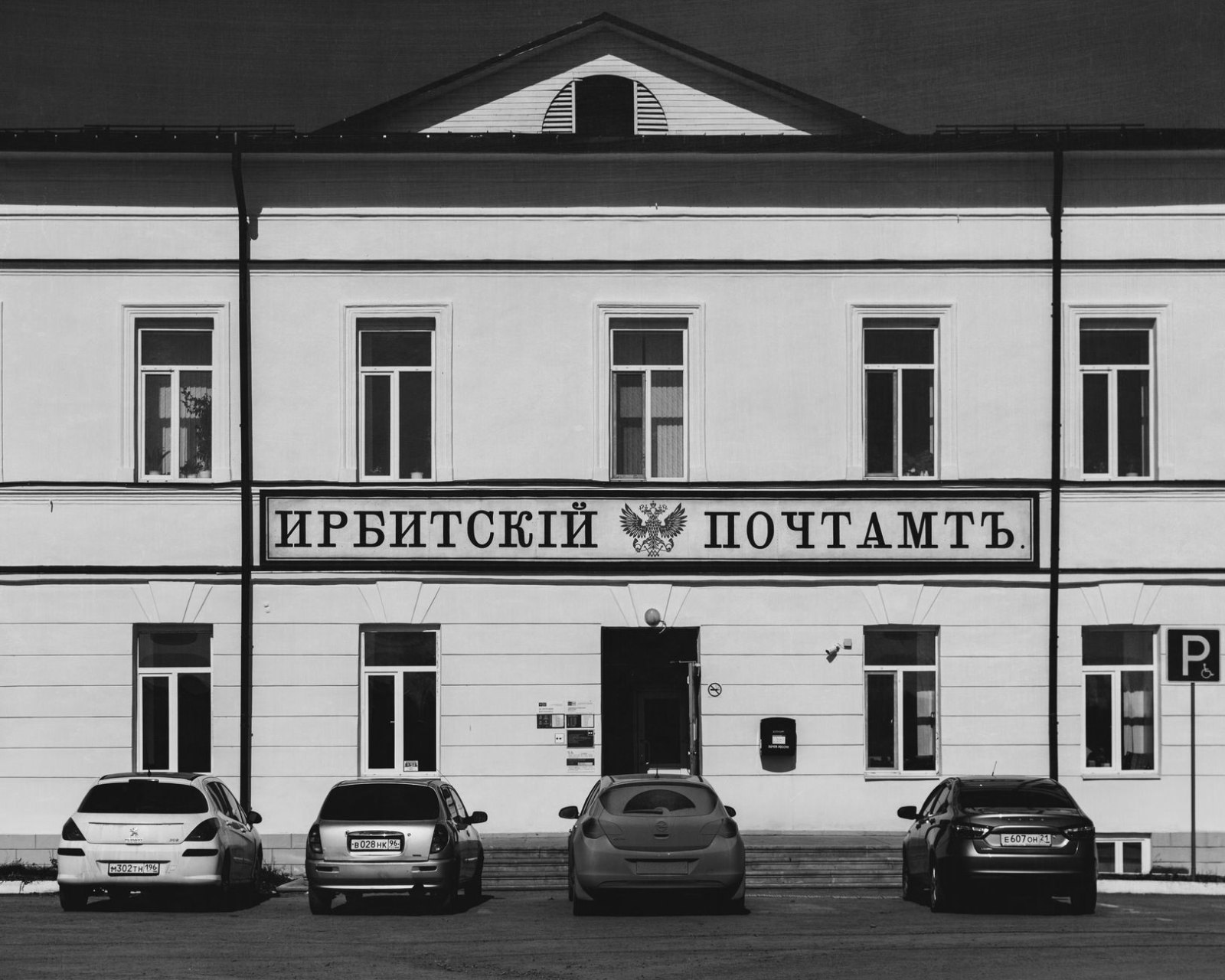 Пожилой мужчина за стойкой центра госуслуг подаёт документы улыбающемуся сотруднику, светлый современный офис